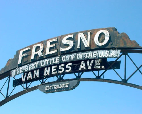 Verweerd metalen boogbord met de tekst Fresno The Best Little City in the USA Van Ness Ave Entrance tegen een blauwe lucht