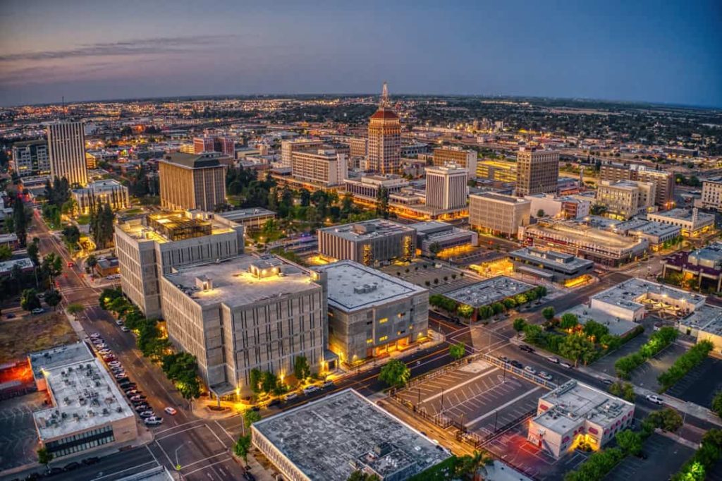 Verlichte hoogbouw en historische torens in het centrum van Fresno in Californië tijdens de blauwe avondschemering, met de stad die zich uitstrekt tot aan de horizon