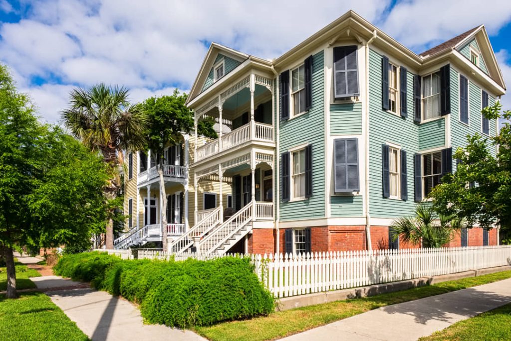 Groen geverfd victoriaans huis met witte veranda's, luiken en een wit hek langs de stoep in een historische wijk van Galveston