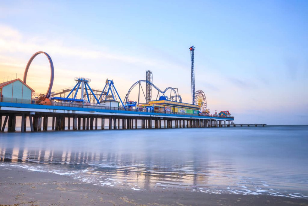 Pretpark op een lange pier met een achtbaan en reuzenrad dat over het water van de Golf van Mexico uitsteekt bij Galveston