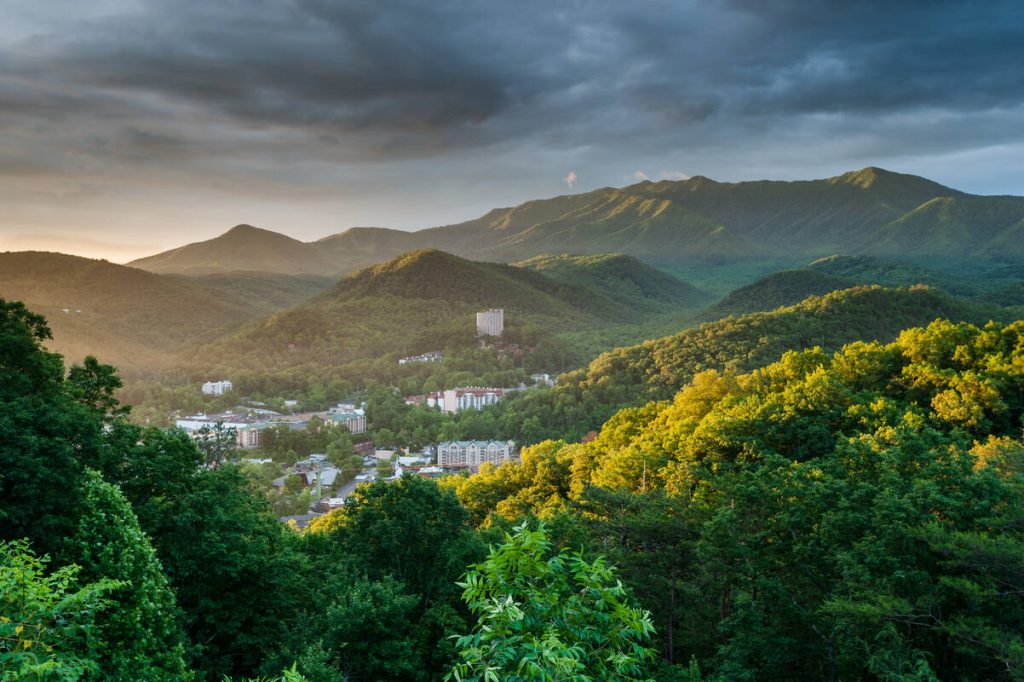 Uitzicht over het stadje Gatlinburg in de Smoky Mountains, omgeven door glooiende beboste heuvels onder een bewolkte lucht bij zonsopkomst