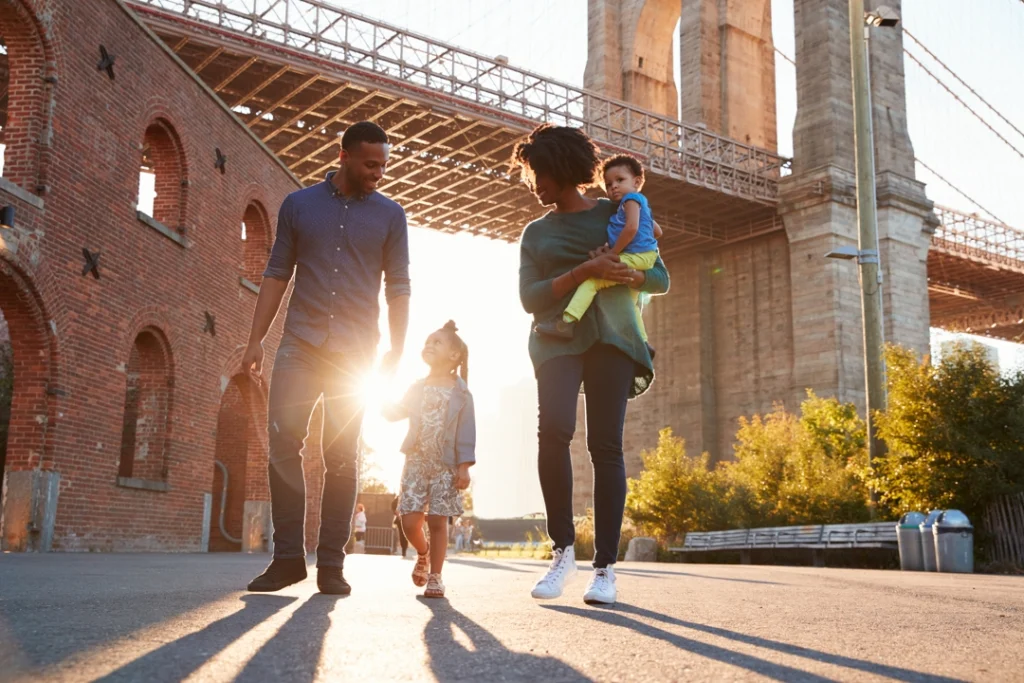 Ouders met twee kinderen wandelen onder de pijlers van de Brooklyn Bridge bij zonsondergang