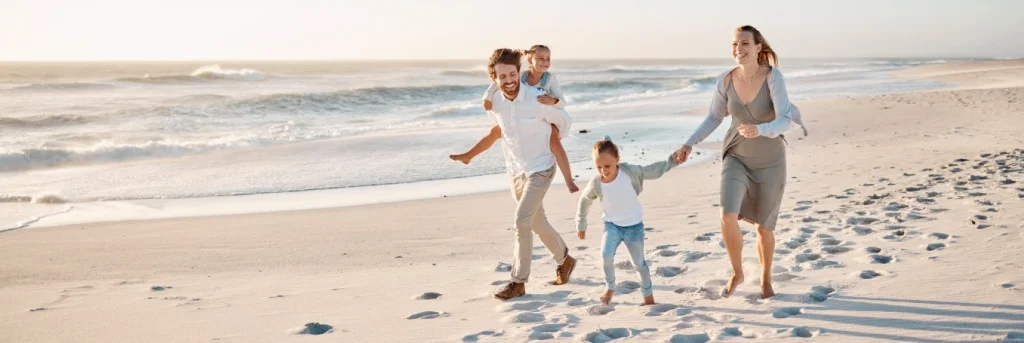 Vader, moeder en twee kinderen lopen lachend over een wit zandstrand tijdens zonsondergang in Florida