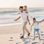 Vader, moeder en twee kinderen lopen lachend over een wit zandstrand tijdens zonsondergang in Florida