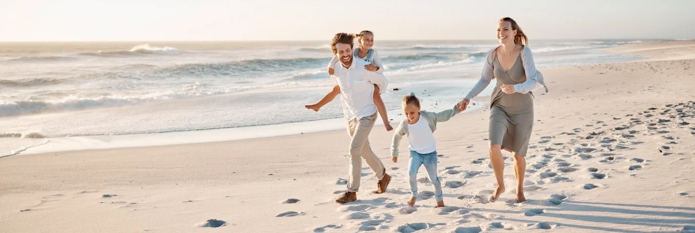 Vader, moeder en twee kinderen lopen lachend over een wit zandstrand tijdens zonsondergang in Florida