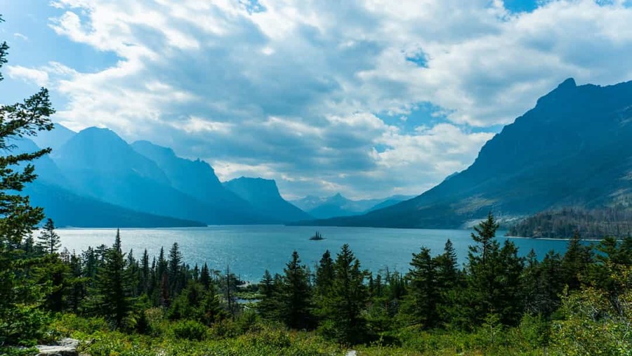 Klein eilandje met bomen midden in het blauwe water van Saint Mary Lake, omgeven door bergtoppen in Glacier National Park