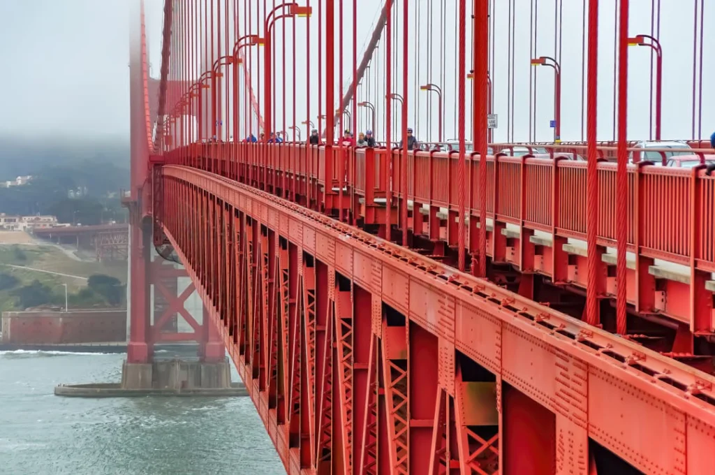 Close-up van de rode stalen constructie en het voetpad van de Golden Gate Bridge, met mist in de verte
