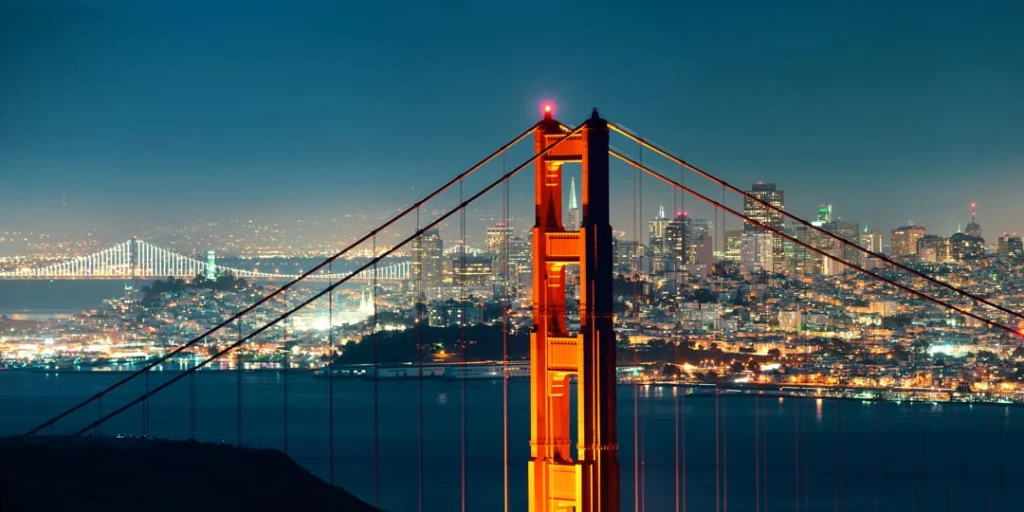 Verlichte toren van de Golden Gate Bridge met de fonkelende skyline van San Francisco op de achtergrond in de avond