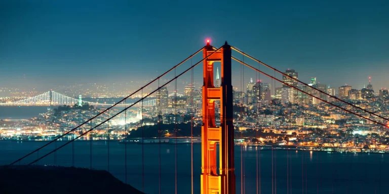 Verlichte toren van de Golden Gate Bridge met de fonkelende skyline van San Francisco op de achtergrond in de avond