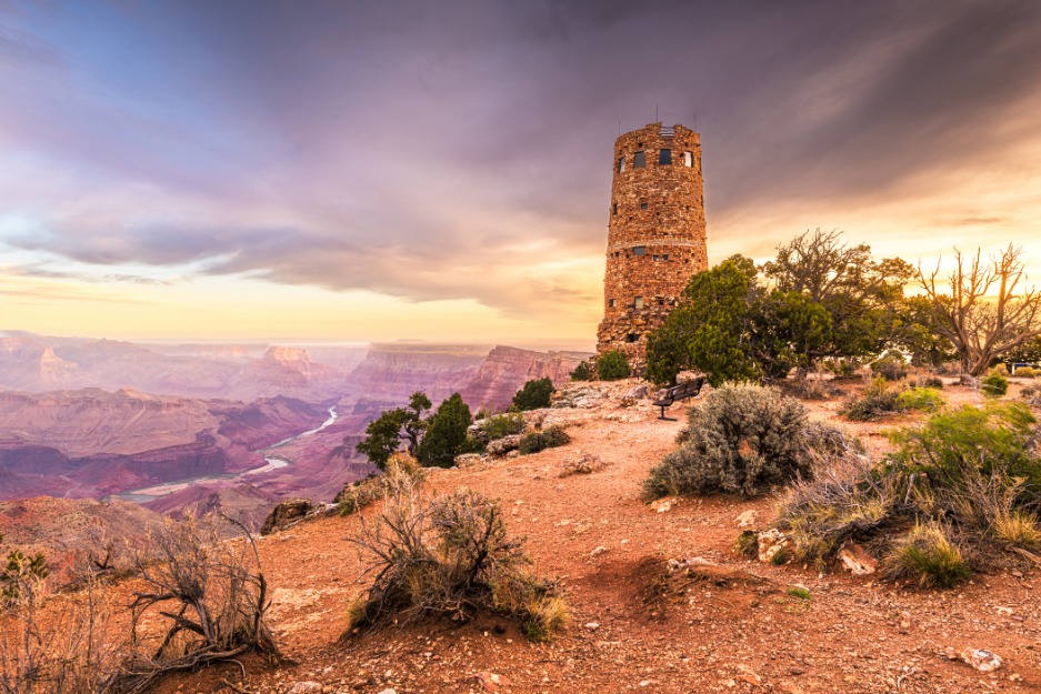 Stenen uitkijktoren op de rand van de Grand Canyon met uitzicht over de gelaagde rotswanden en de Colorado River, onder een dramatische wolkenlucht