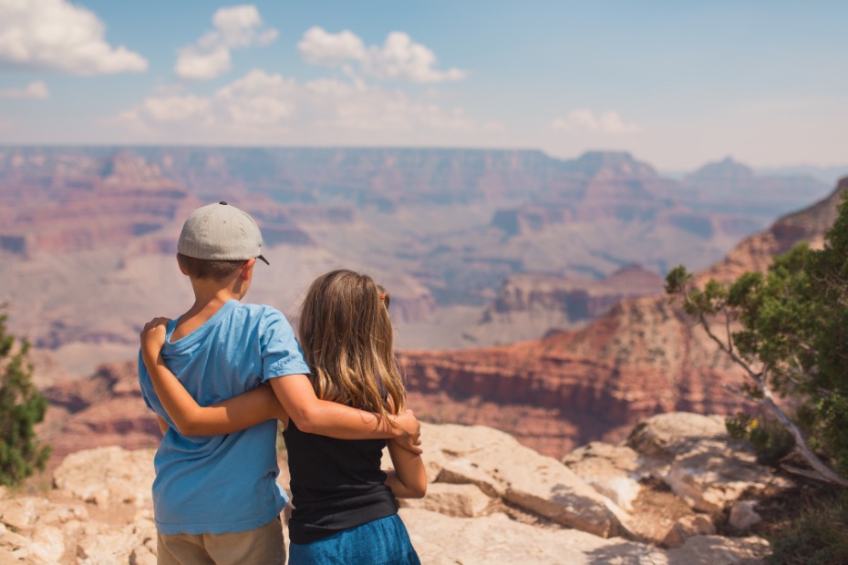 Twee kinderen slaan een arm om elkaar heen terwijl ze uitkijken over de uitgestrekte, roodbruine rotslagen van de Grand Canyon