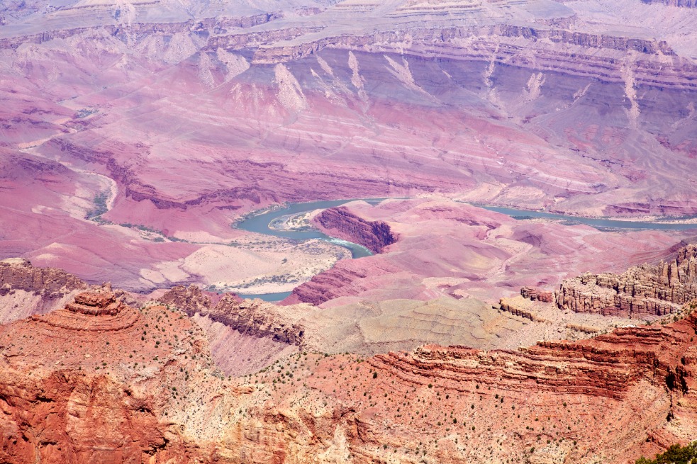 Vogelvluchtperspectief op de paars en roze getinte rotslagen van de Grand Canyon met de Colorado River die er doorheen kronkelt