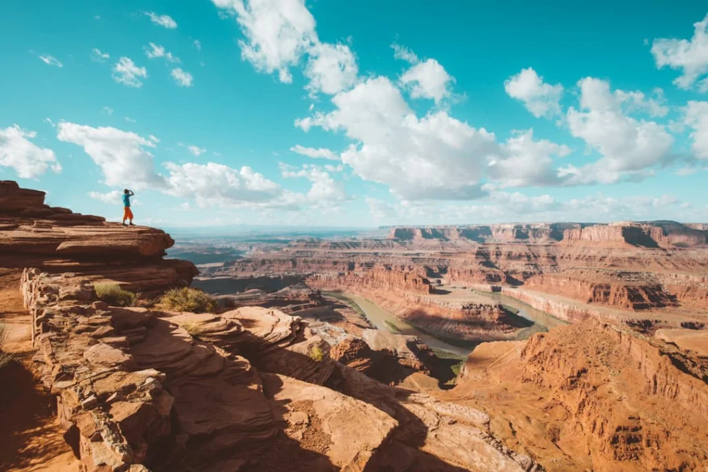 Persoon staat op een rotsrichel en kijkt uit over de gelaagde rotswanden van de Grand Canyon met de rivier diep beneden in Arizona