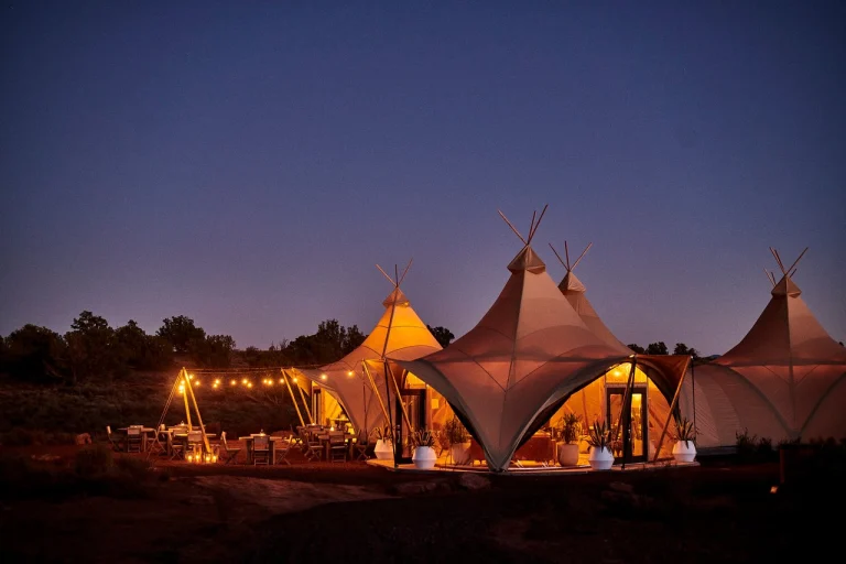 Groep grote verlichte tipitenten met terrasjes en lichtjes in de avondschemering bij een glampingaccommodatie nabij Grand Canyon National Park