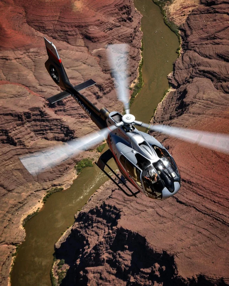 Een helikopter vliegt boven de rotsformaties van de Grand Canyon met de Colorado rivier daaronder kronkelend zichtbaar