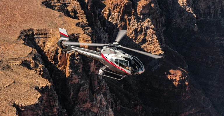 Een witte helikopter vliegt laag over de roodbruine rotswanden van de Grand Canyon