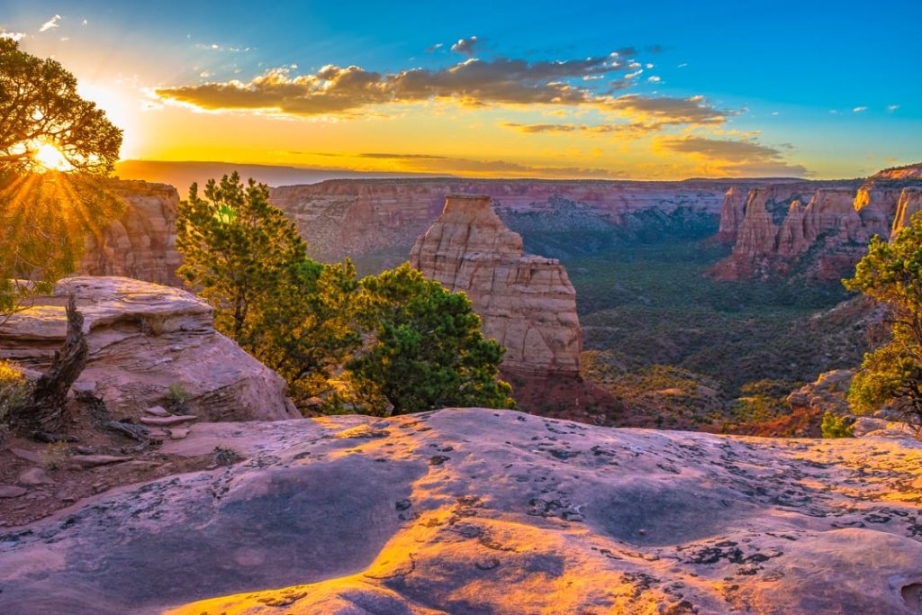 Zonnestralen breken door tussen rode rotstorens in een canyon met jeneverbesstruiken op de voorgrond