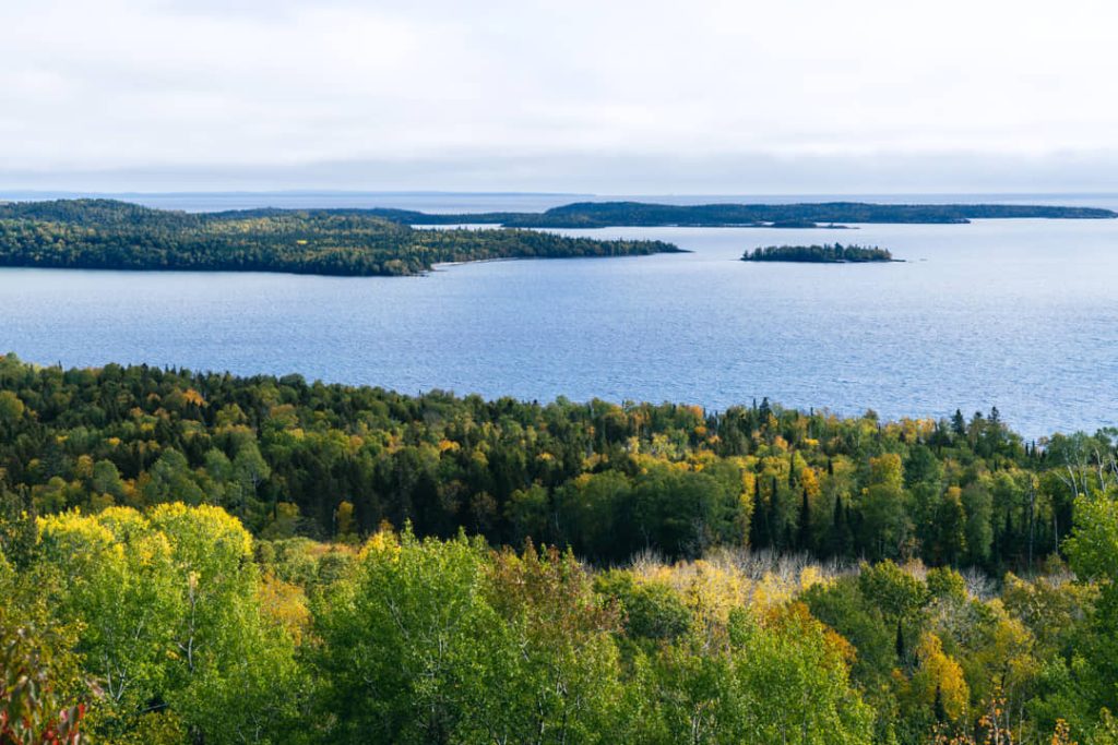 Uitzicht vanaf een heuvel over Lake Superior met beboste eilanden en herfstkleuren op de voorgrond bij Grand Portage