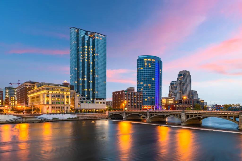 Skyline van Grand Rapids met een blauw verlichte wolkenkrabber en een brug over de rivier bij schemering