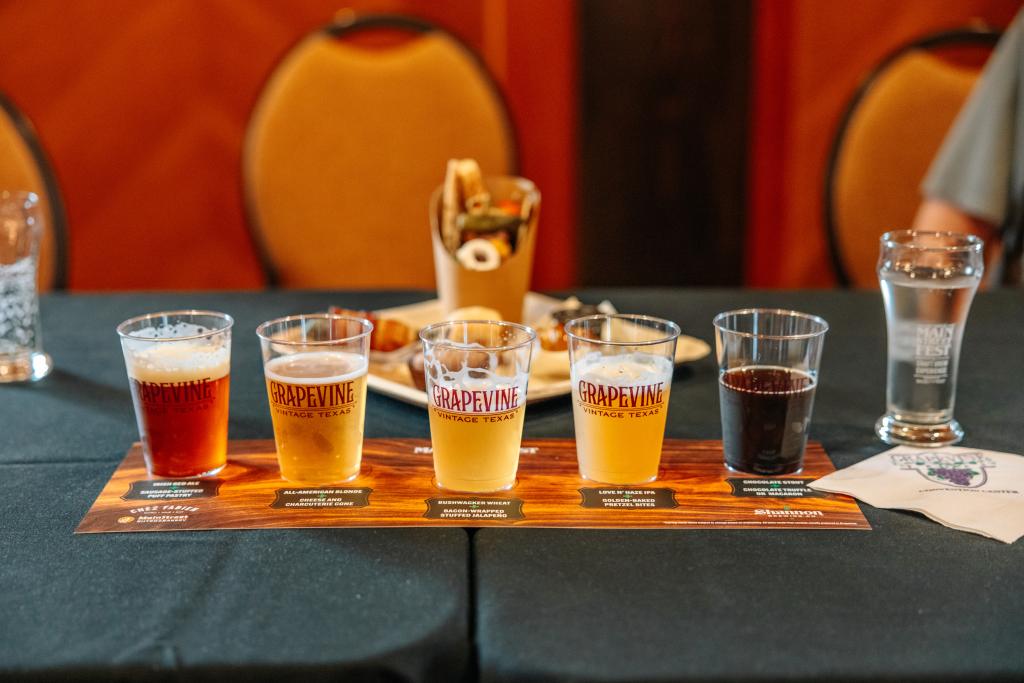 Vijf glazen met verschillende soorten bier op een proefplankje met het opschrift Grapevine Vintage Texas op een tafel