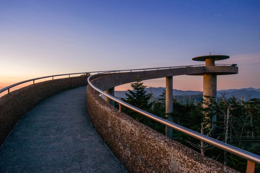 Kronkelend betonnen pad naar de ronde uitkijktoren van Clingmans Dome met bergen aan de horizon bij zonsondergang