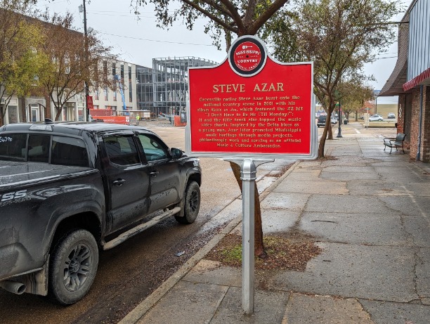 Rood informatiebord van de Mississippi Country Music Trail over zanger Steve Azar langs een straat met een pick-up truck
