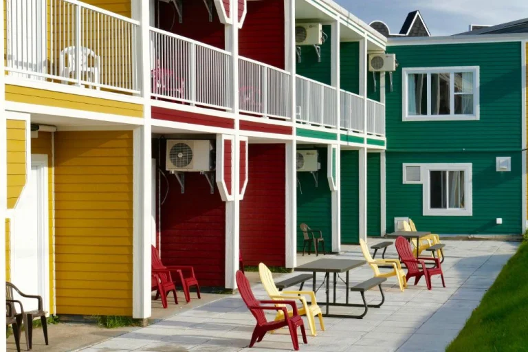 Gele, rode en groene houten gebouwen met witte balkons en een terras met picknicktafels en stoelen in de zon
