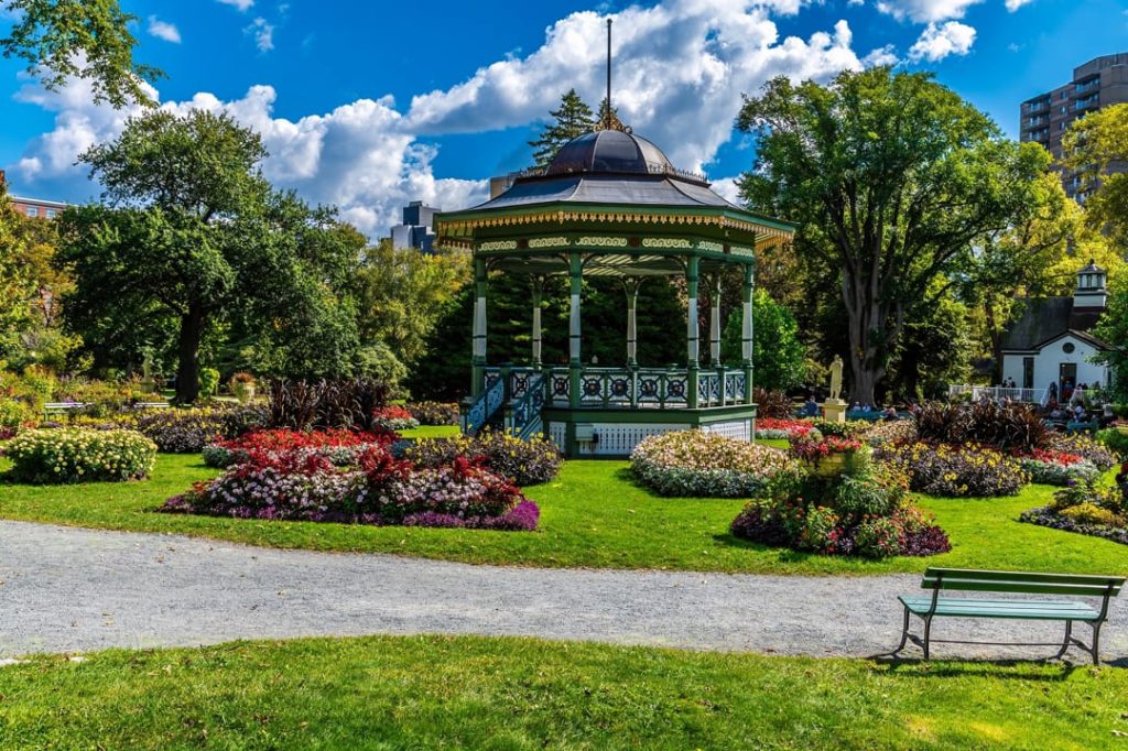 Groenwitte victoriaanse muziekkoepel omringd door kleurrijke bloemperken en groen gazon in de Public Gardens van Halifax onder een blauwe lucht
