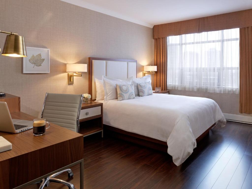 Hotelkamer met een wit bed, een werkbureau met laptop en een raam met uitzicht op de skyline van de stad