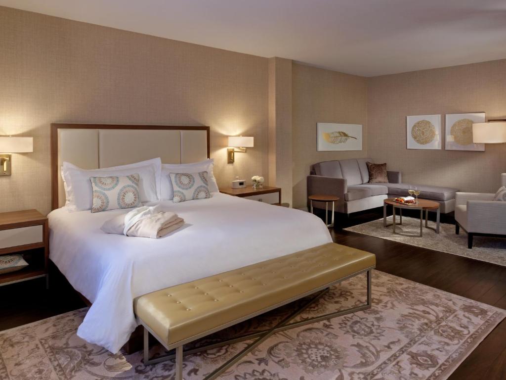 Ruime hotelkamer met een groot wit opgemaakt bed, een zitje en kunst aan de wand in zachte beige tinten