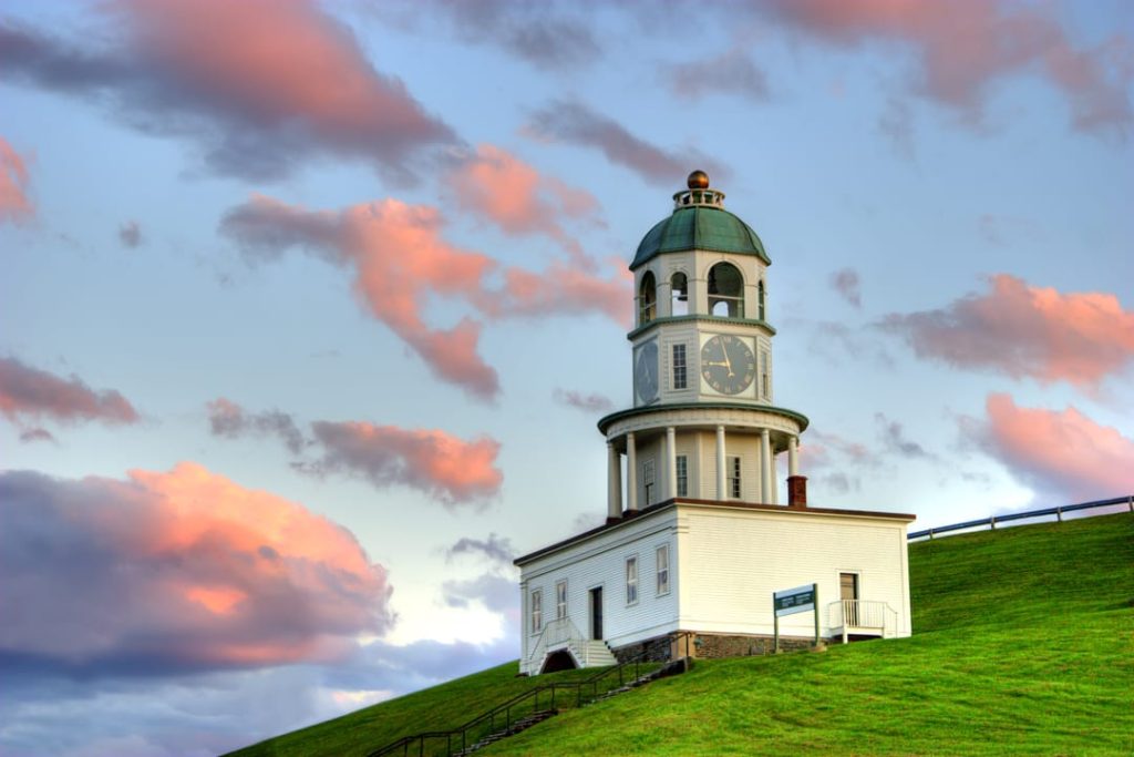 De historische klokkentoren van Halifax met groen koepeldak steekt uit boven een glooiende groene heuvel onder een dramatische roze wolkenlucht