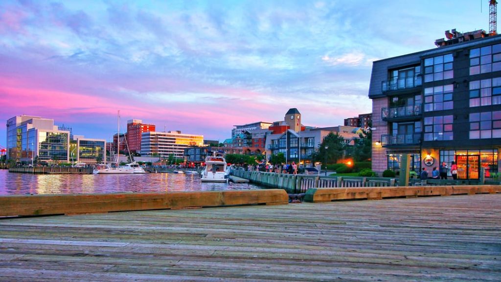 Houten promenade langs de haven van Halifax met boten en wandelaars onder een roze en paarse avondlucht