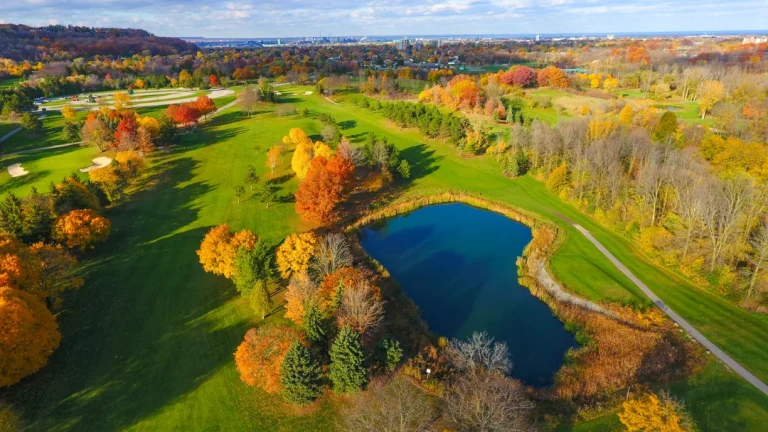 Luchtfoto van een glooiende golfbaan met een blauwe vijver en bomen in oranje en rode herfstkleuren bij Hamilton