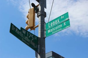 Groene straatnaamborden met de teksten Lenox Avenue, Malcolm X Boulevard en Dr Martin Luther King Jr Boulevard tegen een blauwe lucht in Harlem