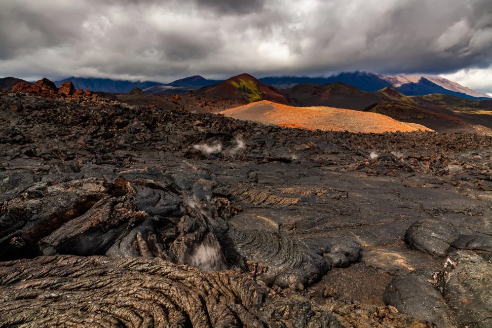 Ruw gestold lavaveld met stoom uit kieren en gekleurde heuvels op de achtergrond bij Mauna Loa op Hawaii
