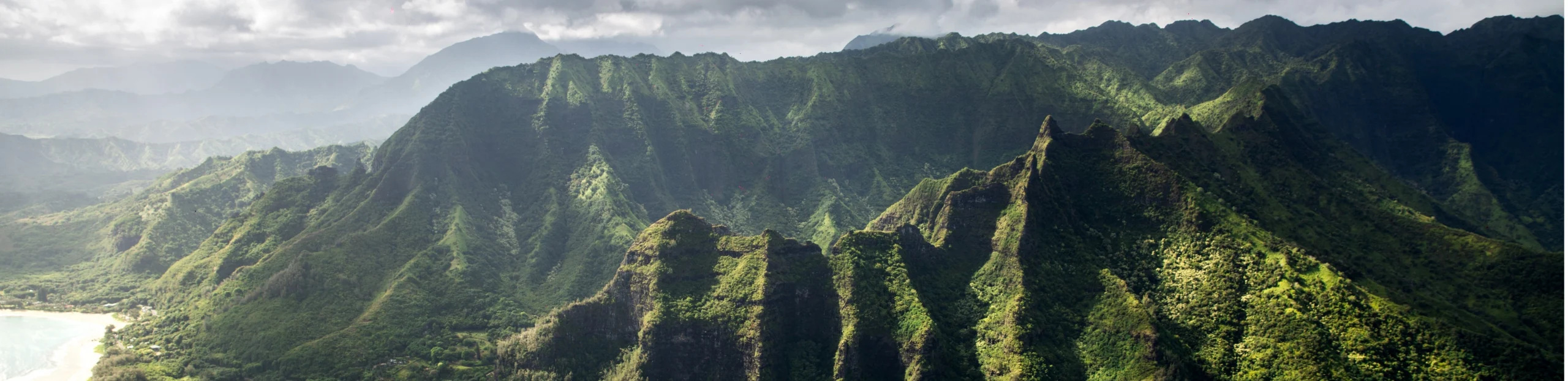 Luchtfoto van een dramatische, groen begroeide bergketen met scherpe pieken langs de kustlijn van Hawaii