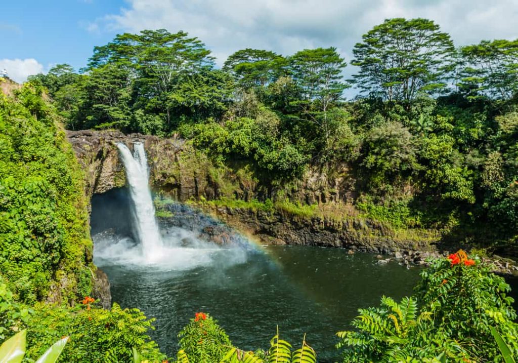 Waterval die in een groene kloof valt met een regenboog zichtbaar in de opspattende nevel bij Rainbow Falls op Hawaii Groot Eiland