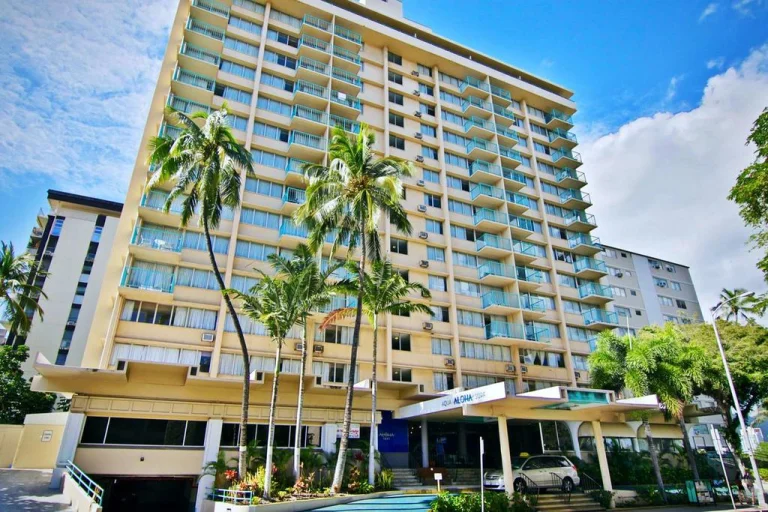 Hoog appartementen- of hotelgebouw met veel balkons, omgeven door palmbomen, onder een blauwe lucht op Oahu, Hawaii