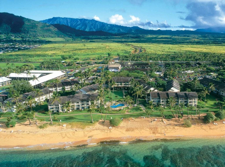 Luchtfoto van een kustresort met zwembad en palmbomen op Kauai, Hawaii, met bergen op de achtergrond