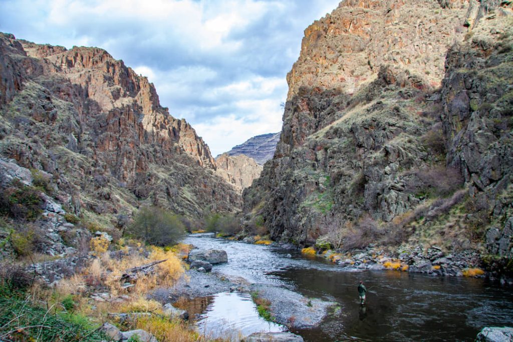 Man vist in een ondiepe rivier die door de diepe kloof van Hells Canyon stroomt met steile rotswanden aan weerszijden