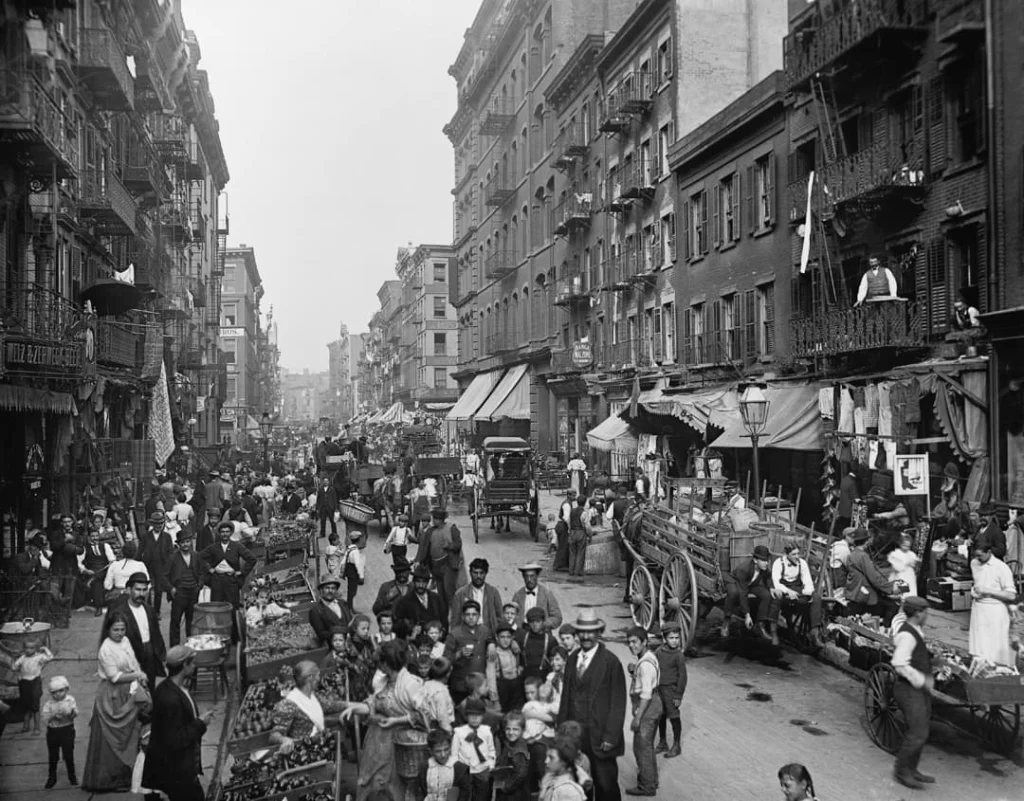 Zwart-witfoto uit het verleden van een drukke straatmarkt met kraampjes en voetgangers in Little Italy, New York