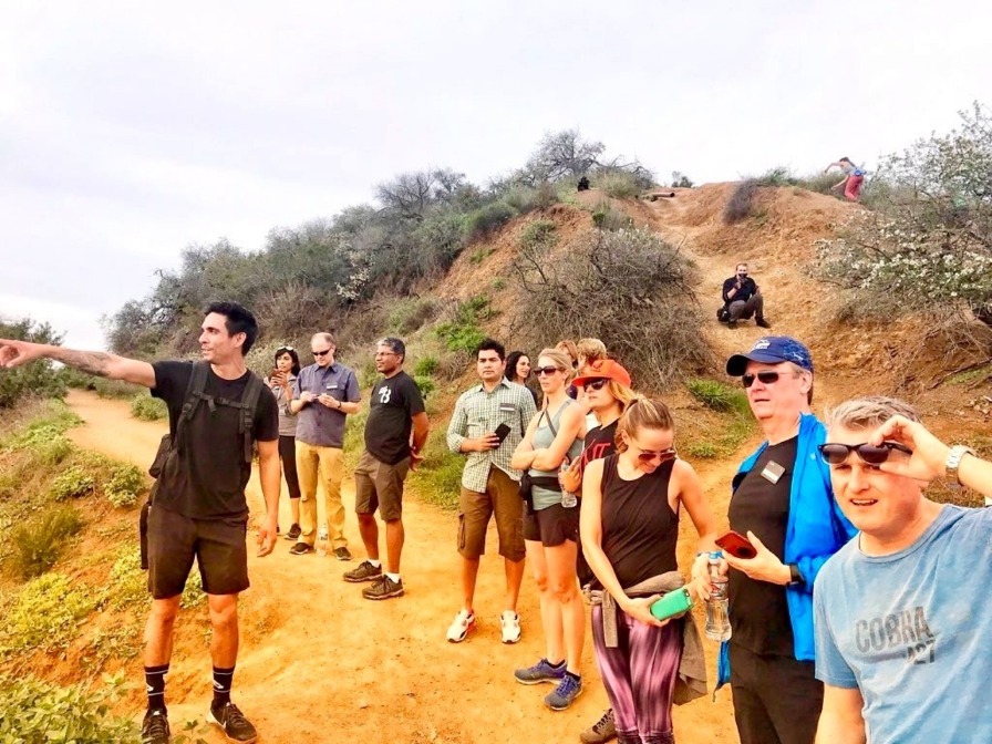 Een gids wijst naar het uitzicht terwijl een groep toeristen op een droog heuvelpad staat tijdens de wandeling naar het Hollywood-teken