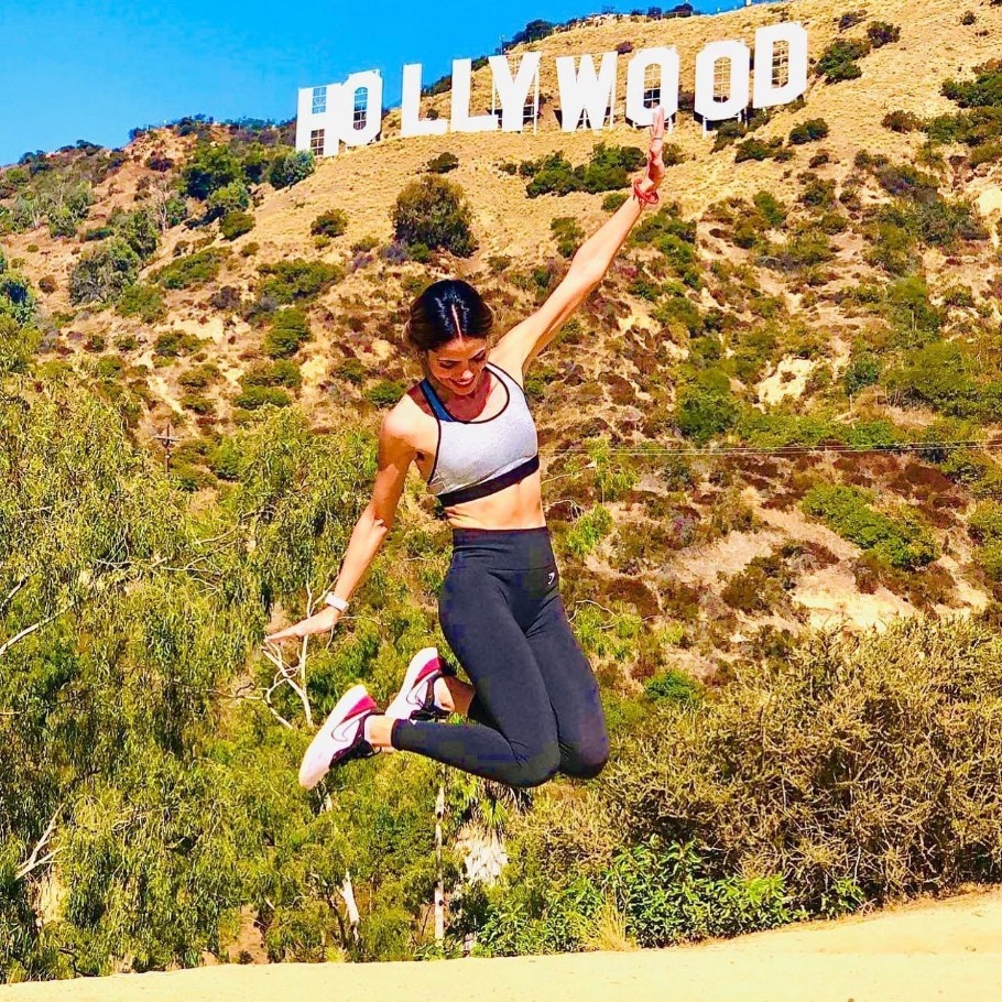 Een vrouw springt enthousiast in de lucht tijdens een wandeling bij het Hollywood-bord op de heuvels van Los Angeles