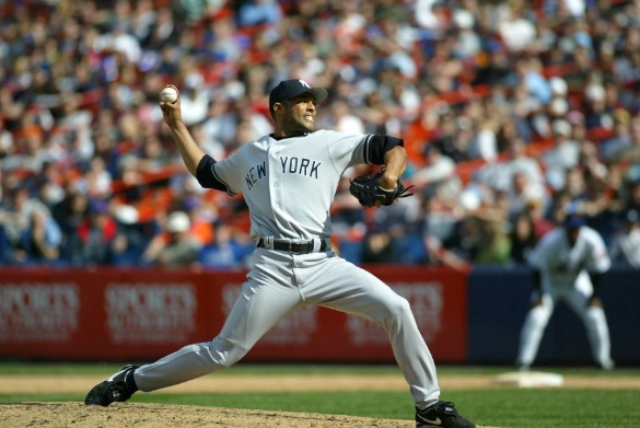 Een werper in Yankees-tenue gooit de bal tijdens een honkbalwedstrijd met publiek op de achtergrond