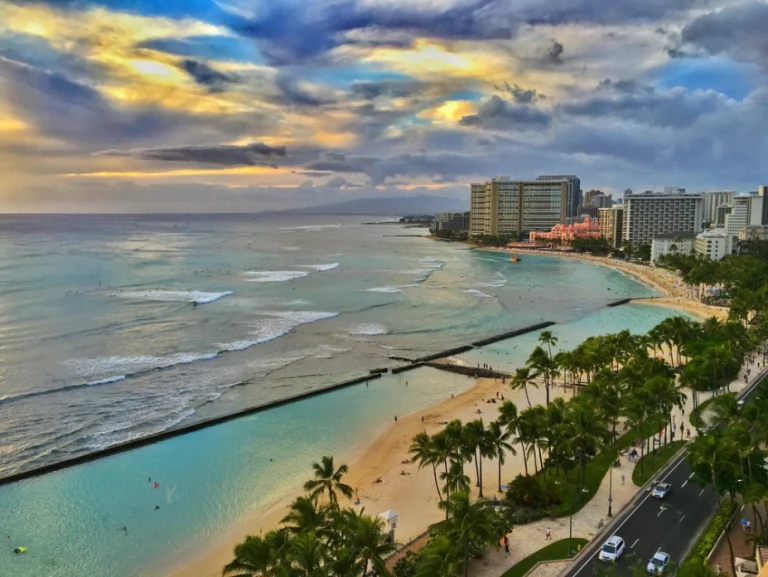 Luchtfoto van Waikiki Beach in Honolulu met golvende zee, palmbomen, hotels en een kleurrijke bewolkte zonsondergang
