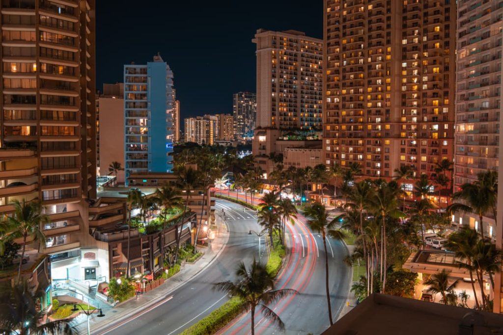 Nachtelijke straat met lichtsporen van rijdende autos tussen verlichte hoogbouw en palmbomen in Waikiki, Honolulu