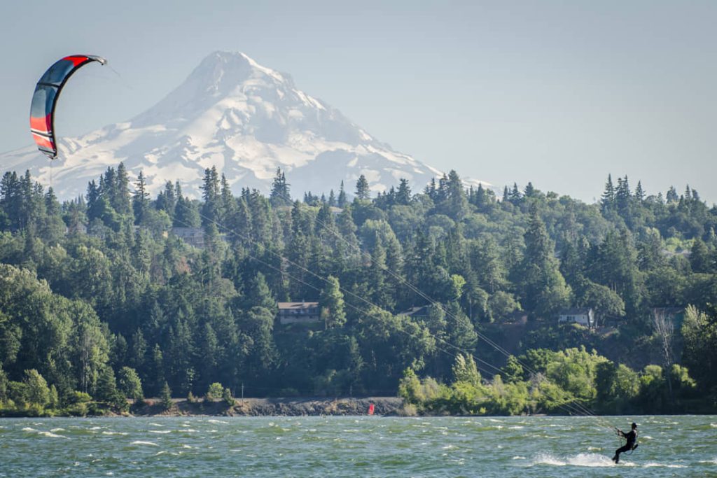 Kitesurfer vaart over het water bij Hood River terwijl de besneeuwde top van Mount Hood boven de bomen uittorent