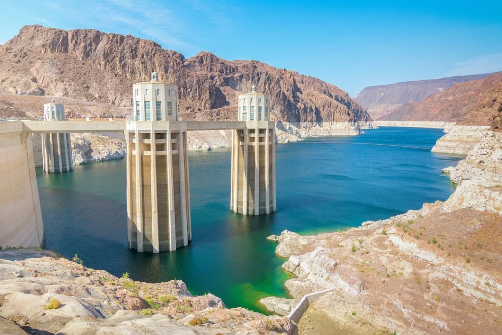 Twee hoge inlaattorens van Hoover Dam steken op uit het turkooisblauwe water van het stuwmeer onder een strakblauwe lucht