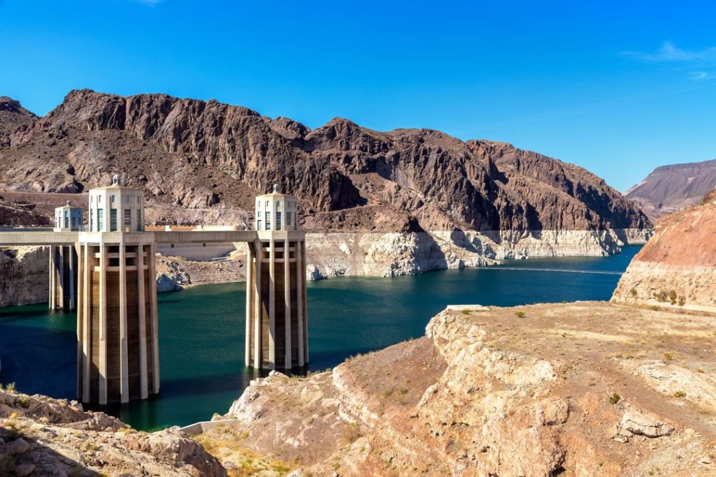 Twee hoge betonnen inlaattorens verbonden door een loopbrug, omringd door het turquoise water van Lake Mead en droge bergen