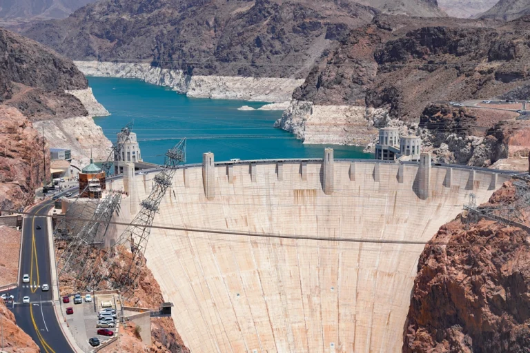 Luchtfoto van de gebogen betonnen Hoover Dam met een turquoise stuwmeer en kale rotswanden op de achtergrond